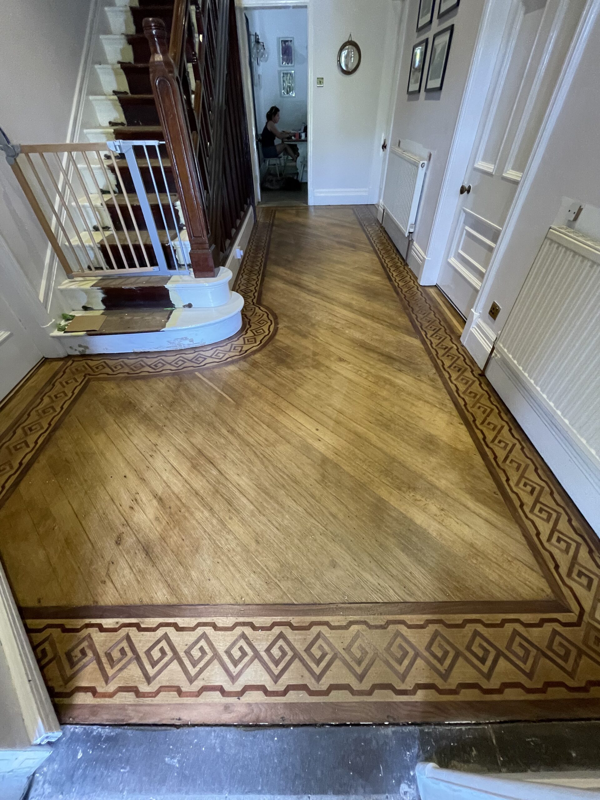 Elegant hallway with geometric patterned wooden flooring and curved staircase