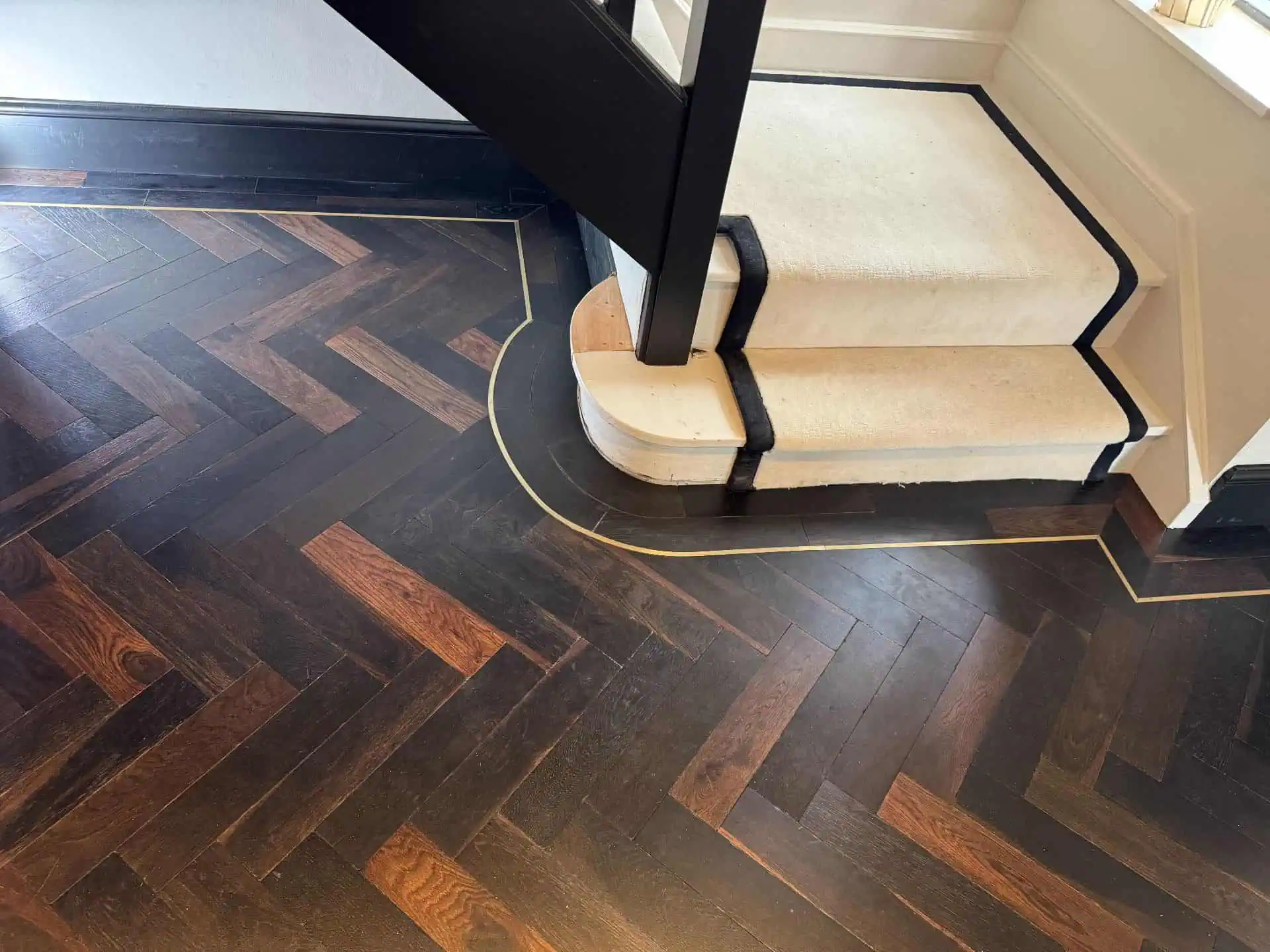 Herringbone wooden flooring with cream staircase and black trim