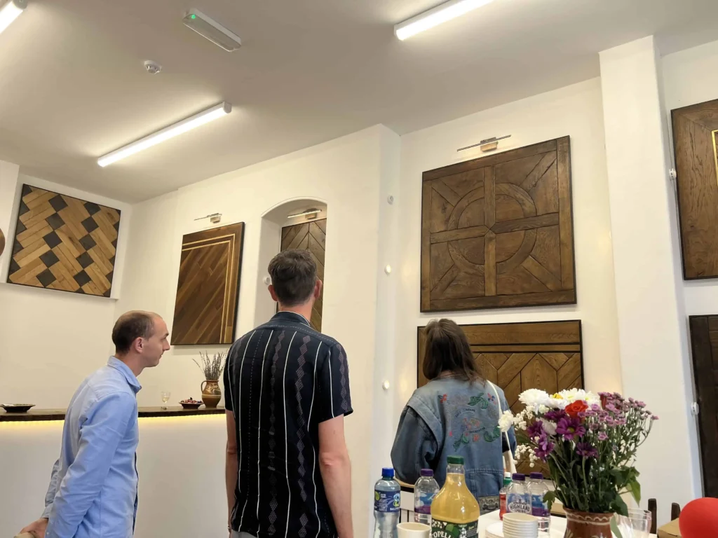 Three people viewing wooden door and floor tile displays in modern showroom