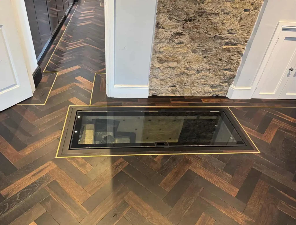 Embedded glass window in herringbone wooden floor with brass trim