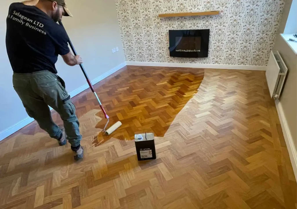 Worker applying wood floor finish with roller brush