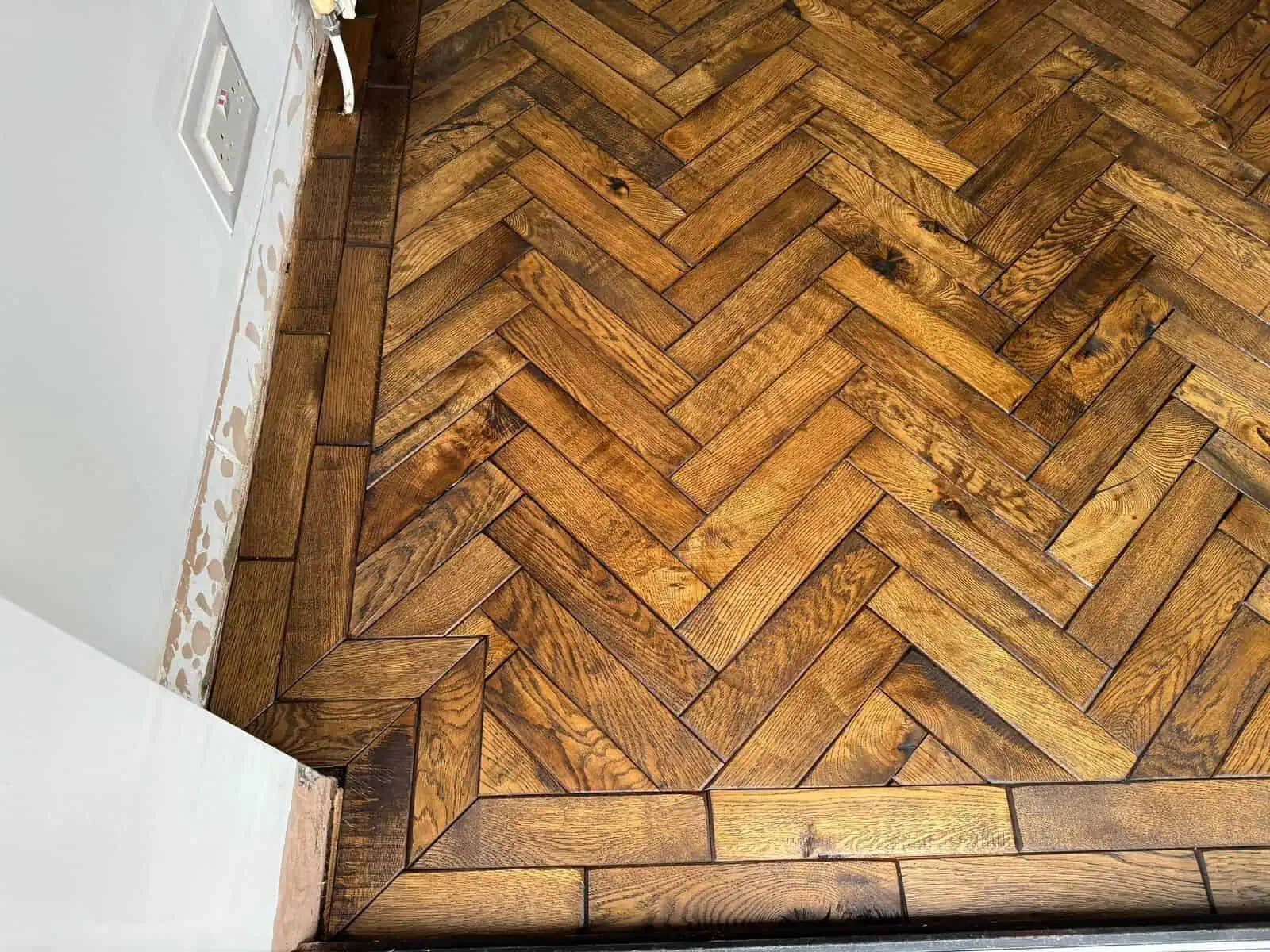 Herringbone parquet wooden floor with white wall and socket