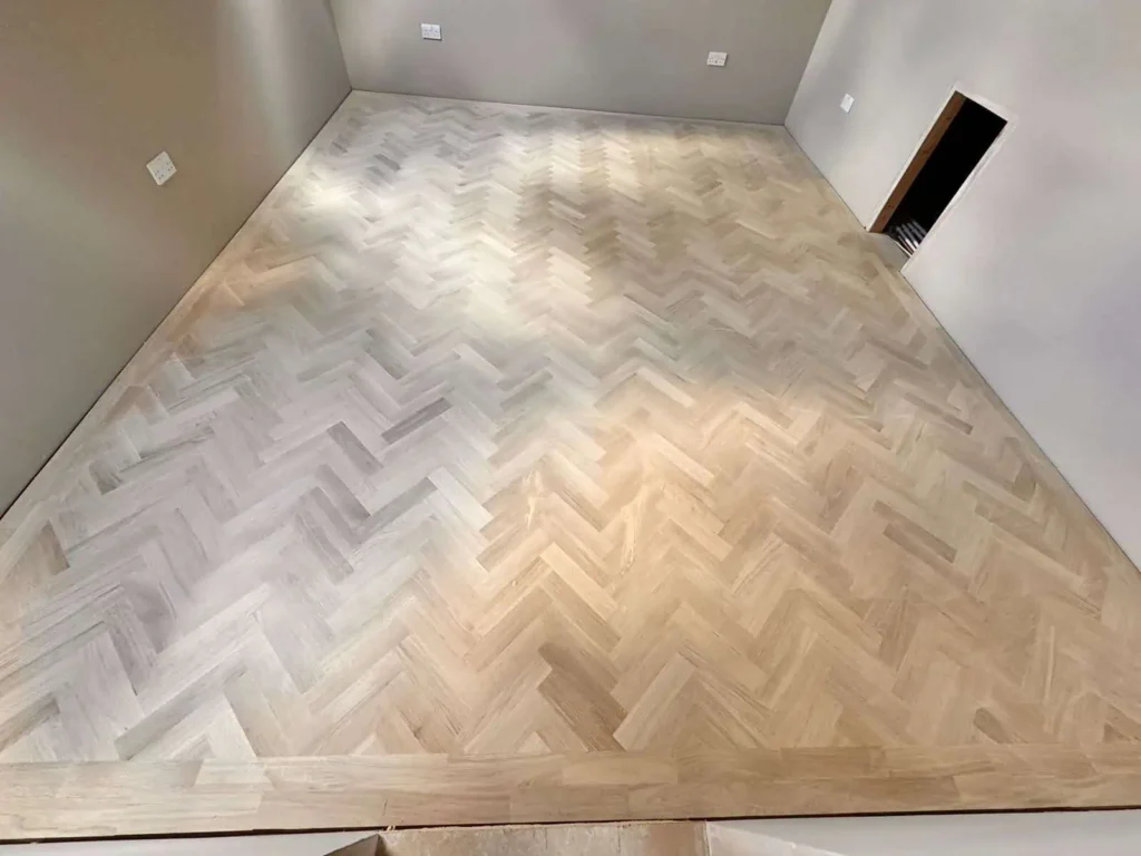 Empty room with light herringbone wood flooring and white walls