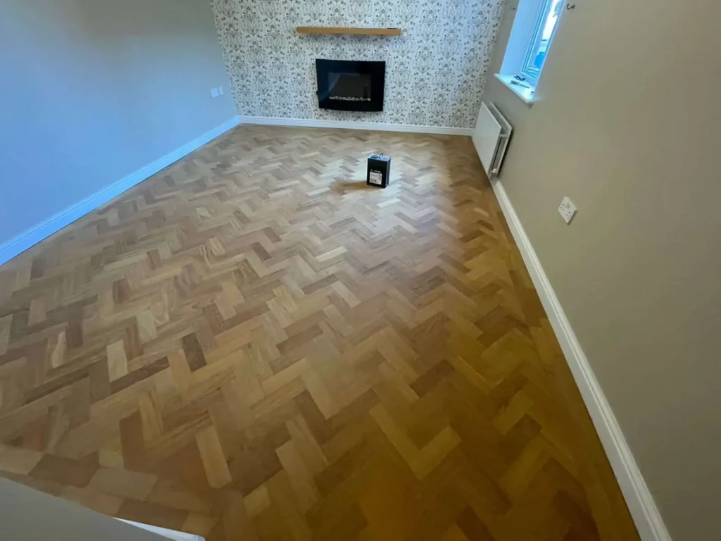 Empty living room with herringbone wood flooring and wall-mounted fireplace