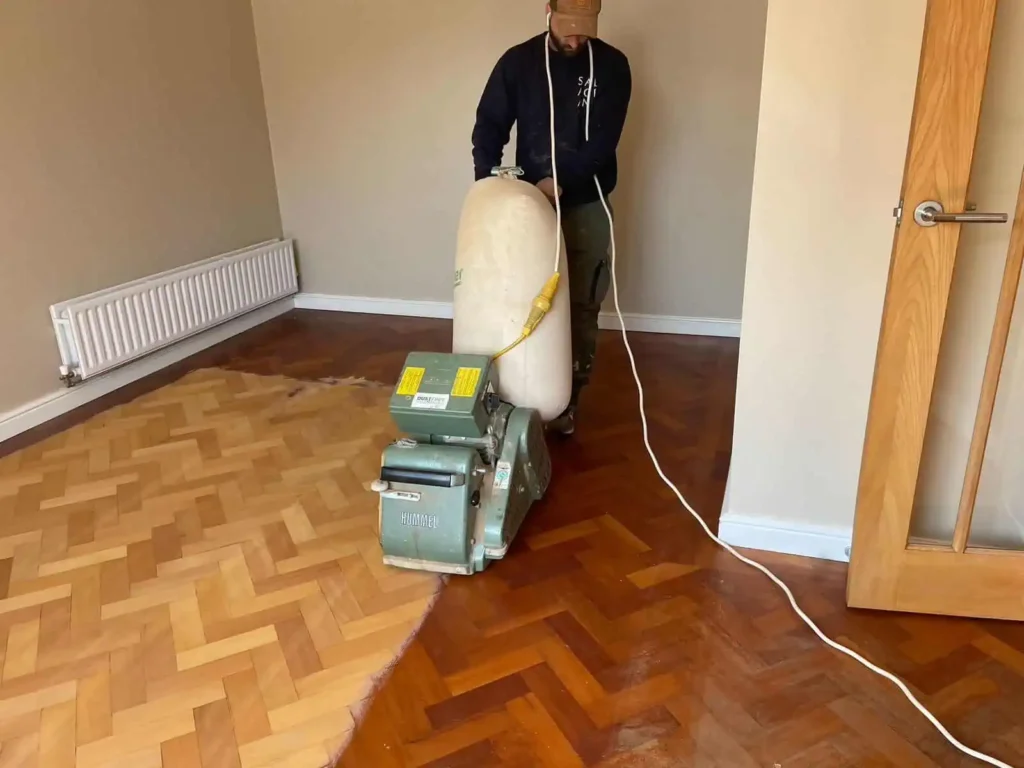 Worker operating floor sanding machine on wooden parquet flooring