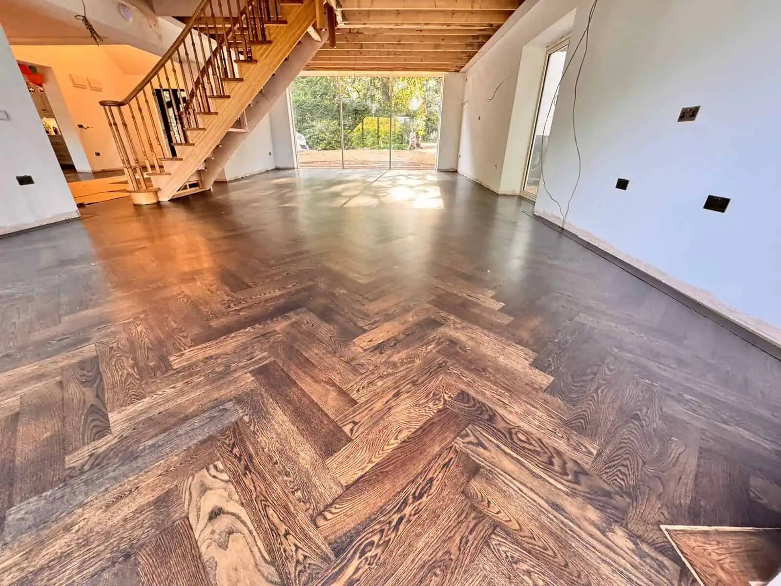 Modern open-plan interior with herringbone wooden flooring and staircase
