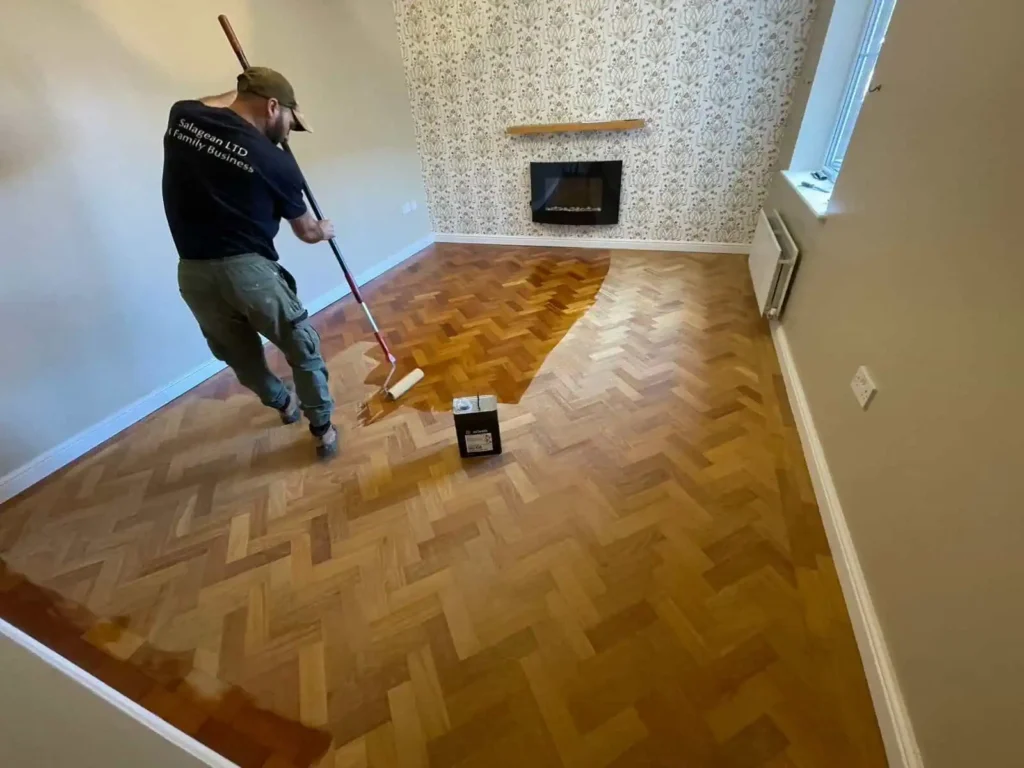 Worker applying finish to herringbone parquet flooring indoors