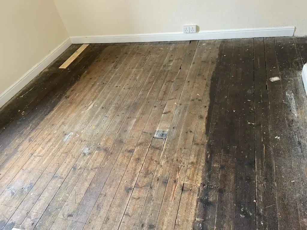 Dirty worn wooden floor with white baseboard trim
