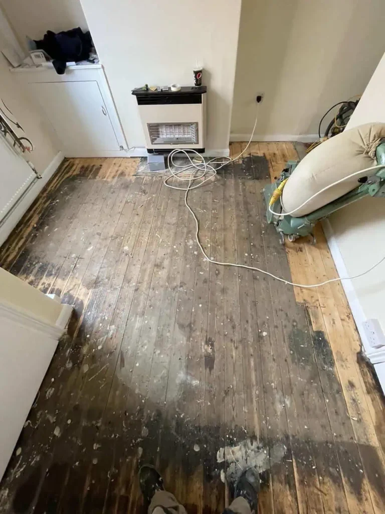 Cluttered room with damaged wooden flooring and heating appliance