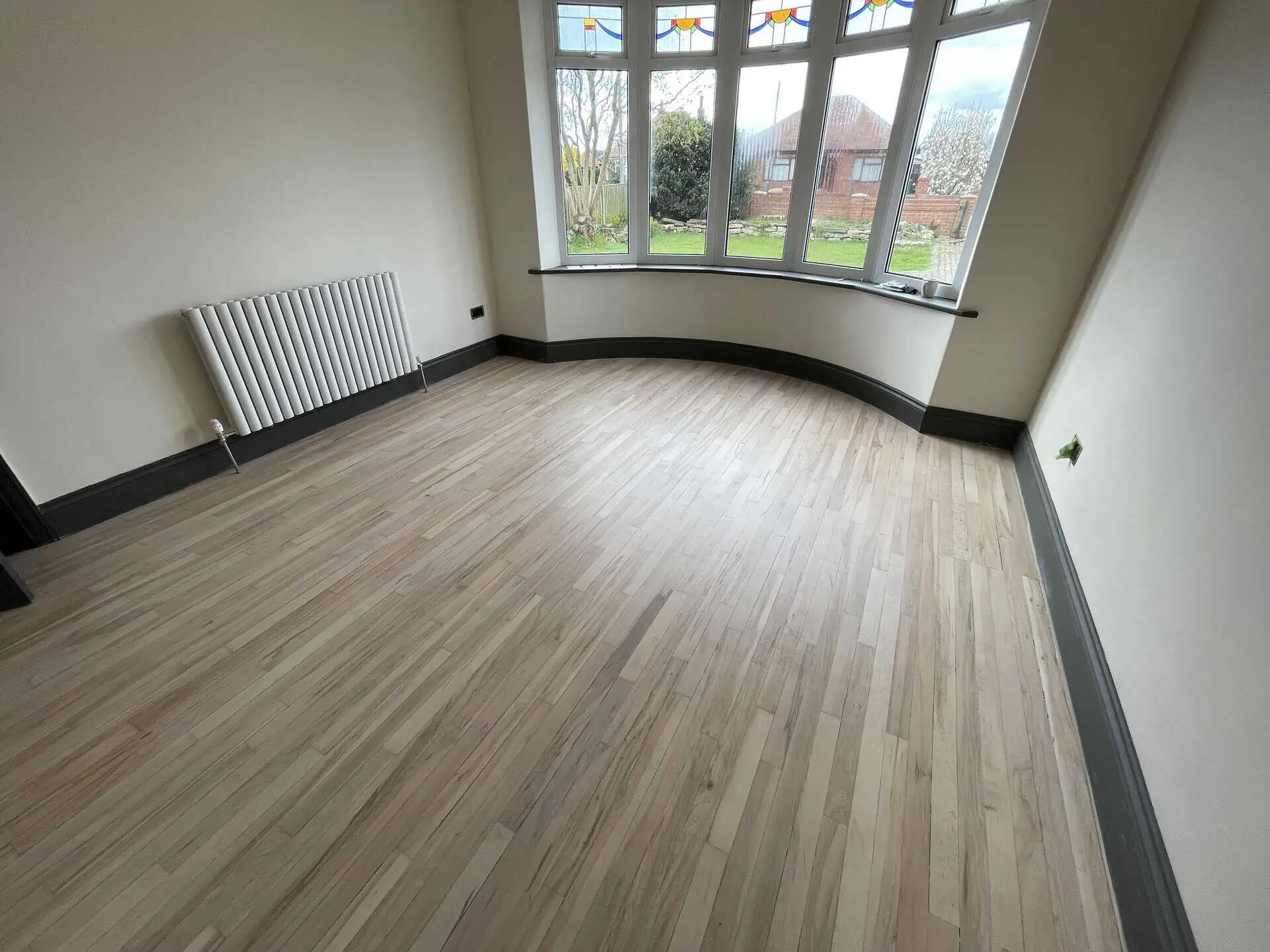 Empty room with wooden flooring, radiator, and bay windows
