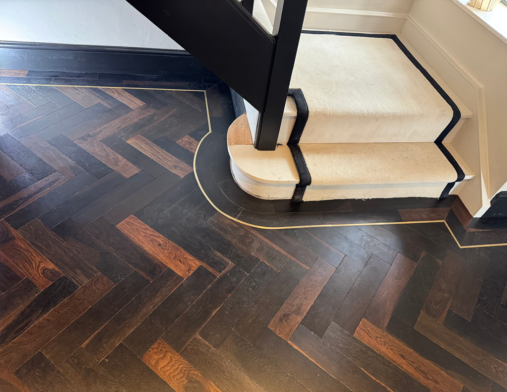 Herringbone wood flooring with black door frame and cream stair runner