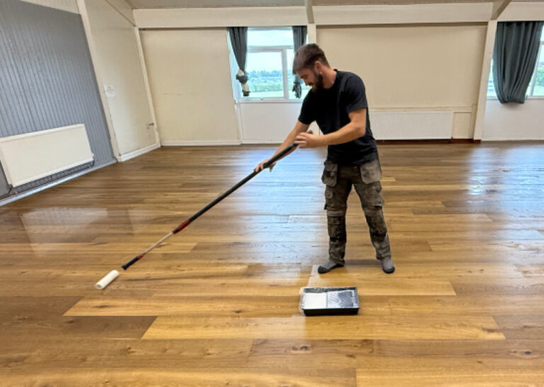 Man applying finish to wooden floor with roller