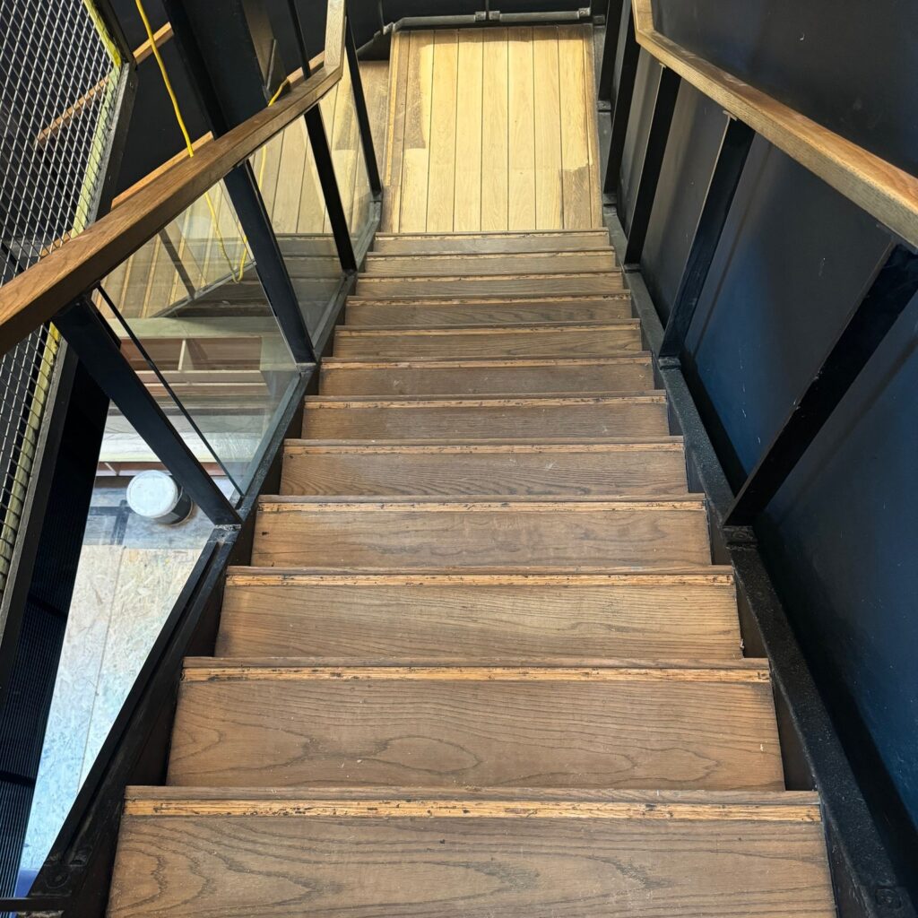 Wooden staircase with handrails ascending between black walls
