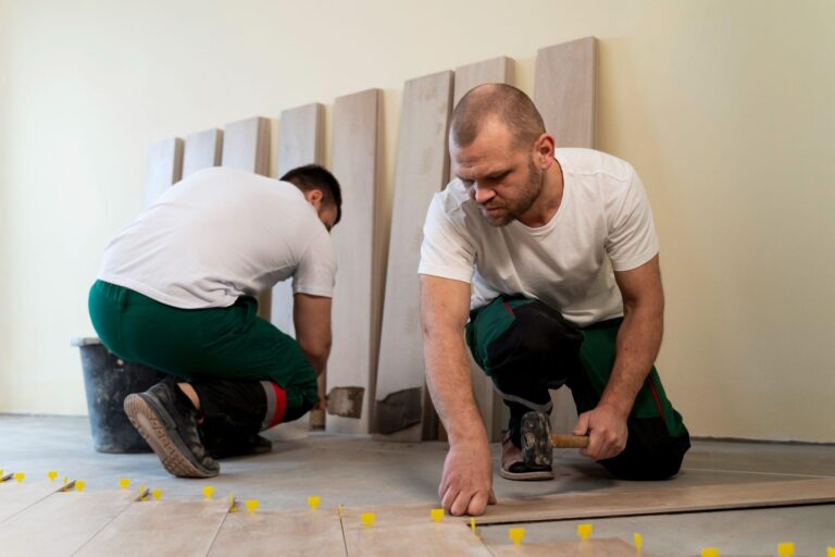 Two workers installing wooden flooring with yellow spacers