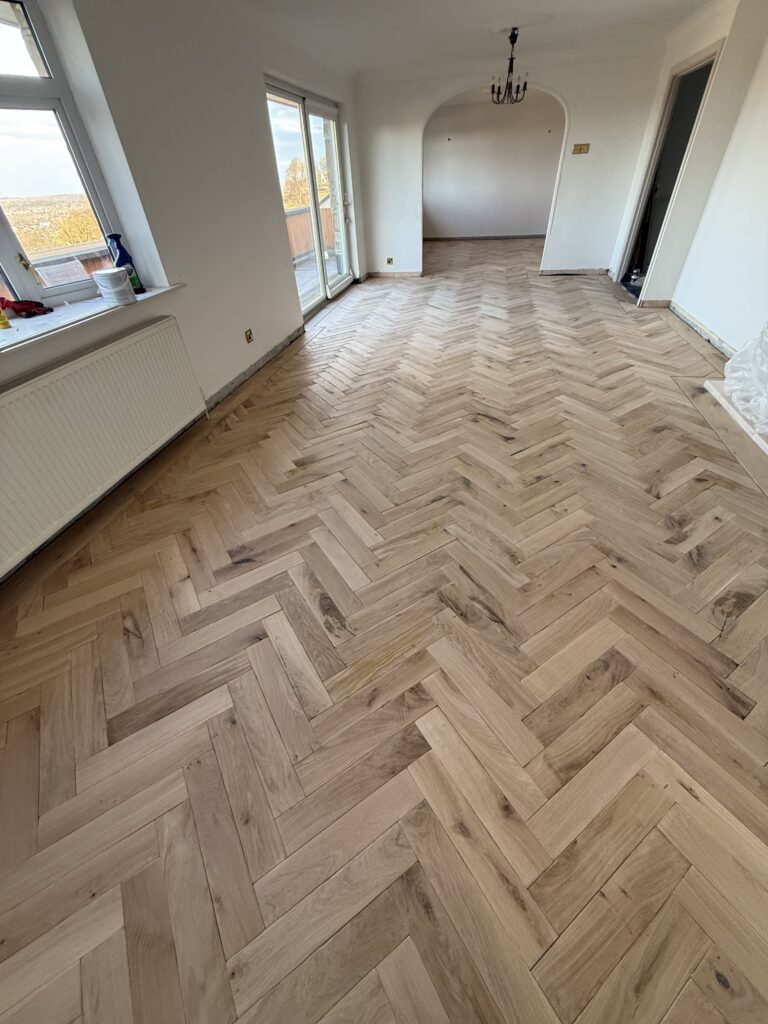 Empty living room with herringbone wood flooring and glass doors